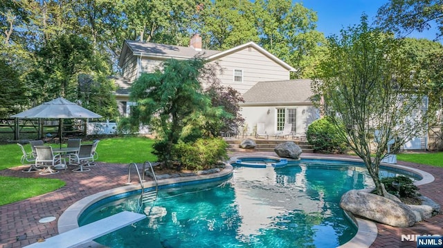 view of pool featuring fence, a yard, a diving board, a pool with connected hot tub, and a patio area