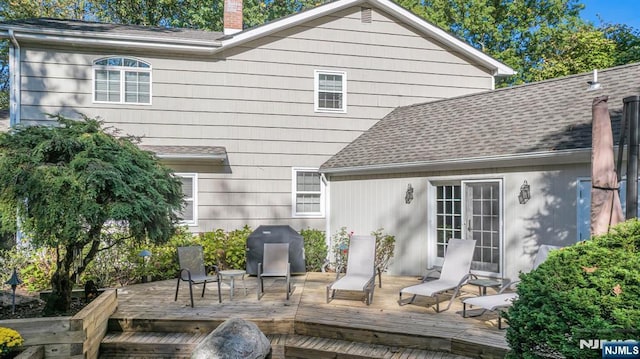 rear view of house featuring a wooden deck, a chimney, and a shingled roof