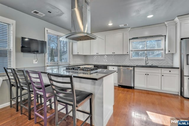 kitchen with sink, a breakfast bar area, appliances with stainless steel finishes, island range hood, and white cabinets