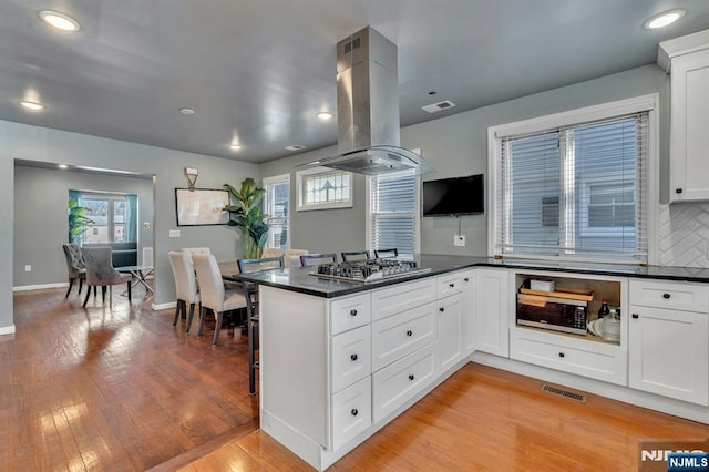 kitchen with island range hood, stainless steel gas stovetop, kitchen peninsula, and white cabinets