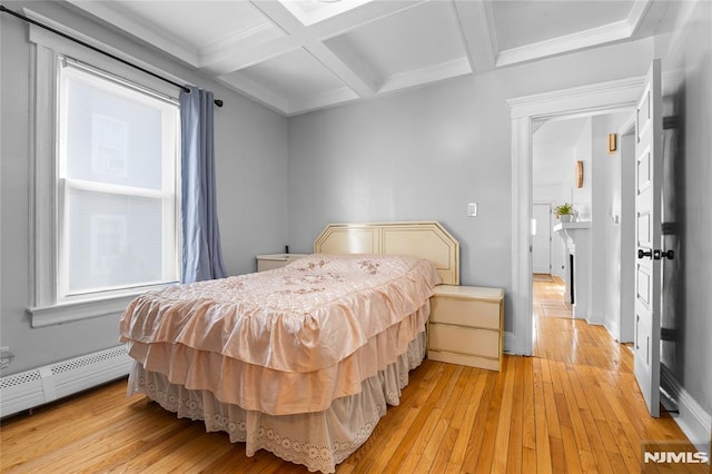 bedroom featuring light wood-type flooring, coffered ceiling, beamed ceiling, and a baseboard heating unit