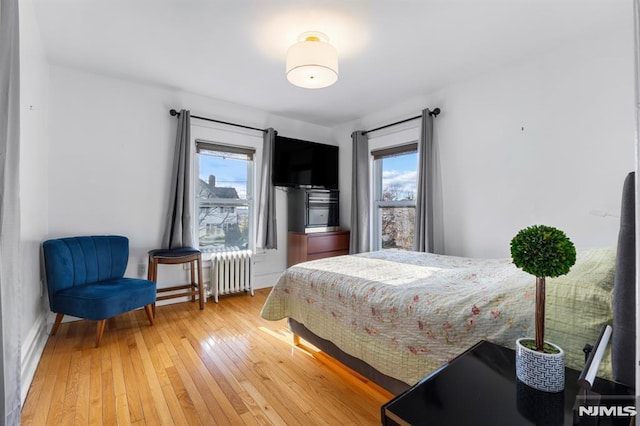 bedroom with radiator heating unit, multiple windows, and wood-type flooring