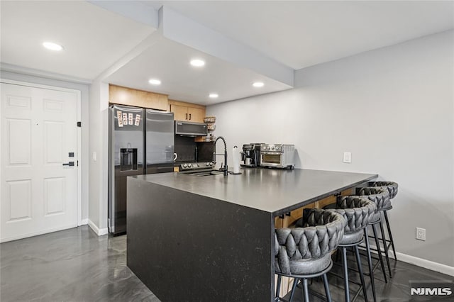 kitchen with stainless steel appliances, light brown cabinetry, decorative backsplash, a kitchen bar, and sink