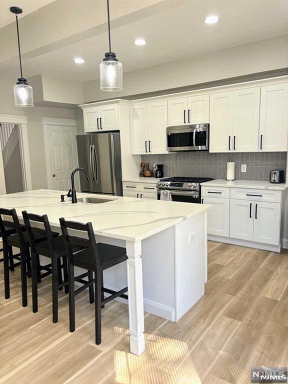 kitchen with decorative light fixtures, stainless steel appliances, white cabinets, and an island with sink