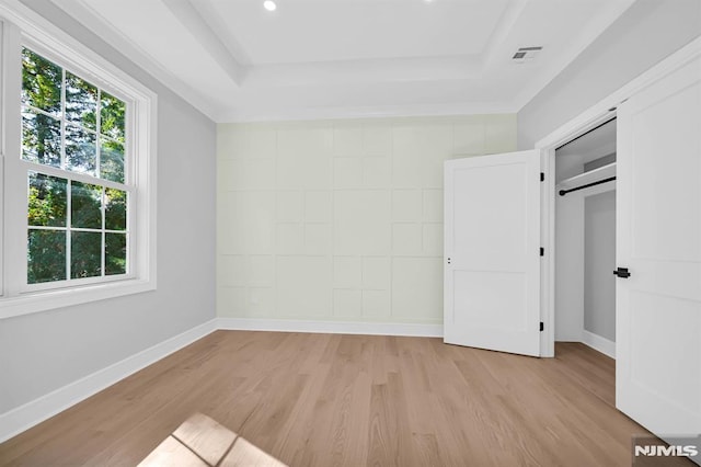 unfurnished bedroom with light hardwood / wood-style floors, a closet, and a tray ceiling