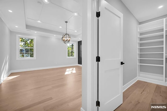 hallway featuring a raised ceiling, light hardwood / wood-style floors, and a chandelier