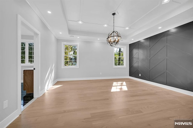 spare room with light hardwood / wood-style floors, a chandelier, a raised ceiling, and plenty of natural light