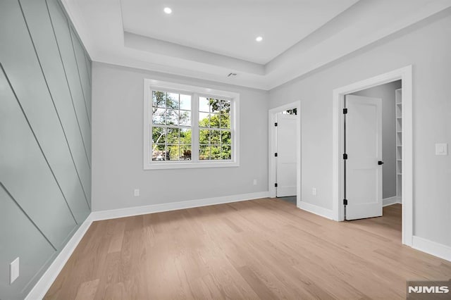 unfurnished bedroom with a raised ceiling, light hardwood / wood-style floors, and a spacious closet