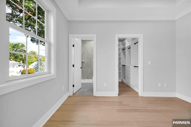 unfurnished bedroom featuring a walk in closet, light hardwood / wood-style flooring, ensuite bathroom, and multiple windows