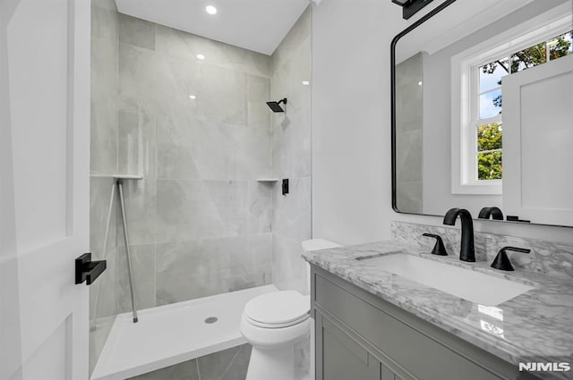 bathroom featuring toilet, tiled shower, and vanity