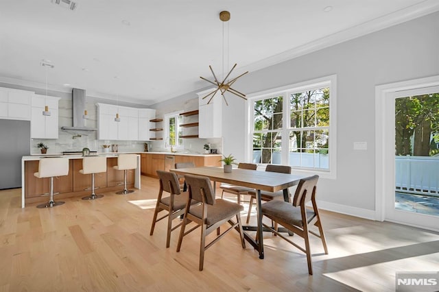 dining room with light wood-type flooring, ornamental molding, and a chandelier