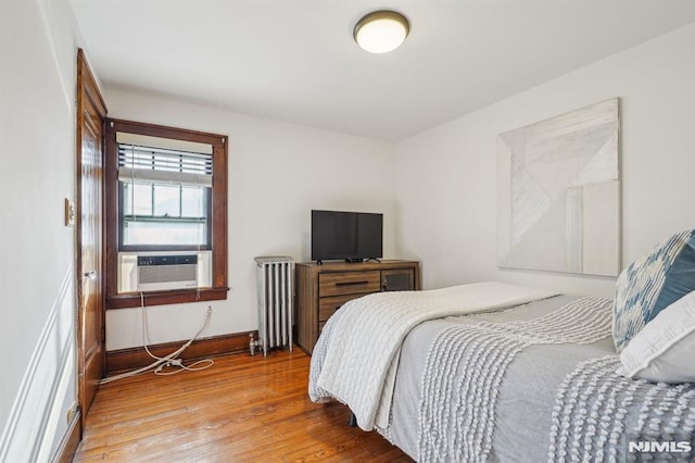 bedroom featuring cooling unit, radiator heating unit, and wood-type flooring