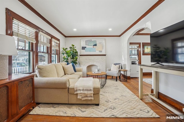 living room featuring a healthy amount of sunlight, hardwood / wood-style floors, ornamental molding, and a fireplace