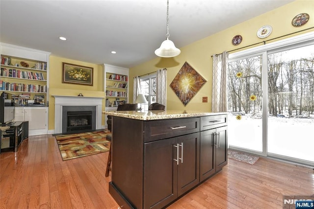 kitchen with pendant lighting, a center island, dark brown cabinetry, light stone countertops, and light wood-type flooring