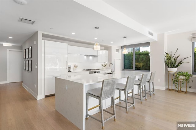 kitchen with sink, decorative light fixtures, white cabinetry, and an island with sink