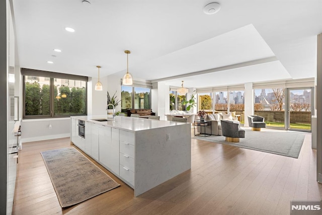 kitchen featuring white cabinets, a kitchen island with sink, light hardwood / wood-style flooring, and pendant lighting