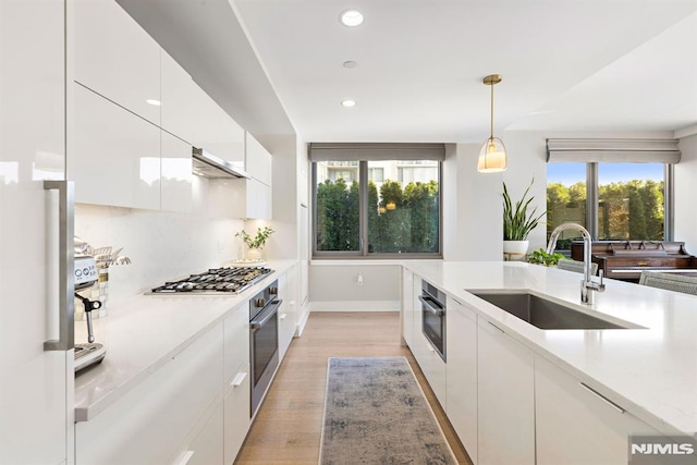 kitchen featuring sink, white cabinets, light hardwood / wood-style floors, pendant lighting, and appliances with stainless steel finishes