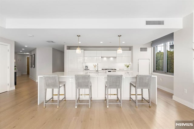 kitchen with light hardwood / wood-style floors, hanging light fixtures, white cabinetry, and a kitchen bar