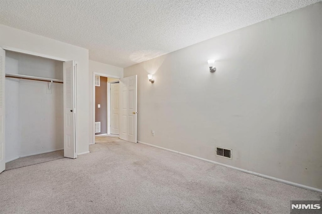 unfurnished bedroom with a textured ceiling, a closet, and light colored carpet