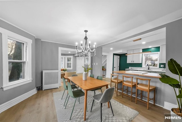 dining room with a notable chandelier, radiator, light hardwood / wood-style floors, ornamental molding, and sink