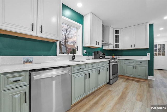 kitchen featuring stainless steel appliances, sink, white cabinetry, light hardwood / wood-style floors, and wall chimney range hood