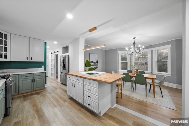 kitchen featuring wooden counters, a barn door, appliances with stainless steel finishes, white cabinetry, and decorative light fixtures