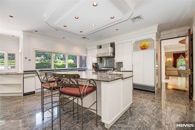 kitchen with a kitchen breakfast bar, dark stone countertops, wall chimney exhaust hood, white cabinets, and a center island