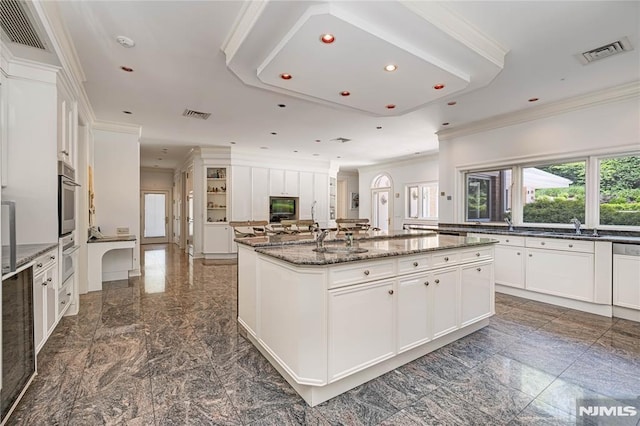 kitchen with a spacious island, white cabinets, dark stone countertops, a raised ceiling, and crown molding