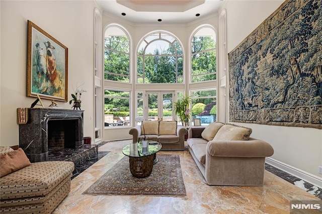 living room featuring a tray ceiling, a towering ceiling, french doors, a high end fireplace, and crown molding