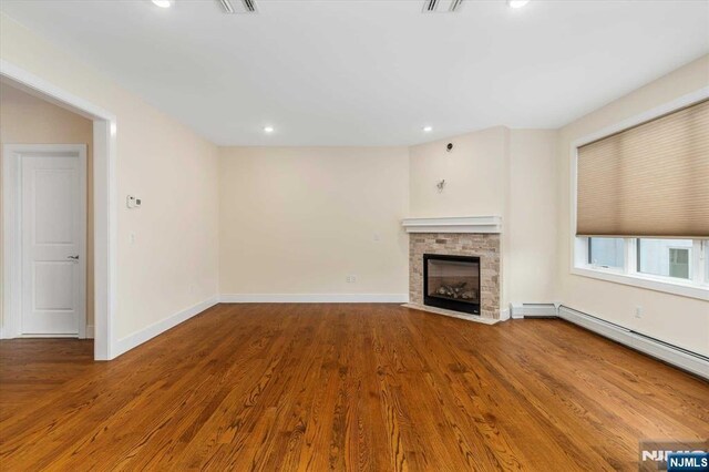 unfurnished living room featuring wood finished floors, a stone fireplace, baseboards, baseboard heating, and recessed lighting