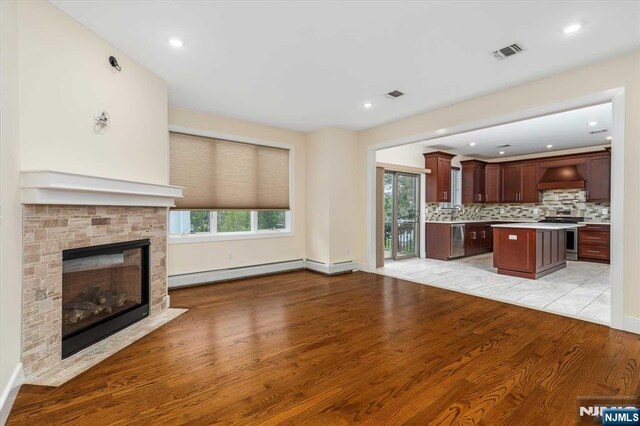 unfurnished living room with visible vents, a stone fireplace, light wood-style flooring, and a baseboard radiator