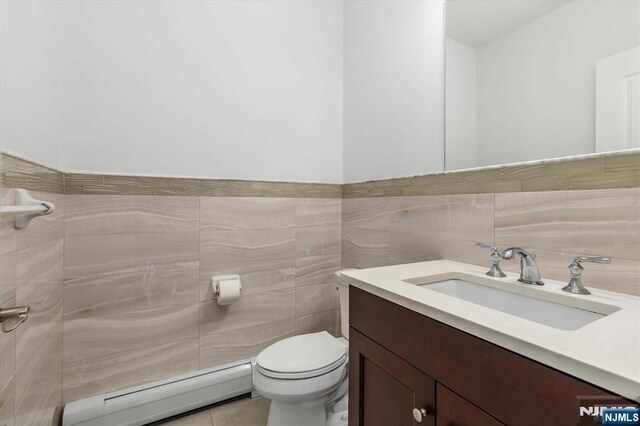 half bathroom featuring vanity, tile patterned flooring, toilet, tile walls, and baseboard heating