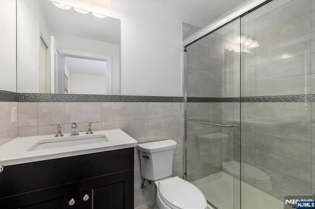 bathroom featuring vanity, a stall shower, toilet, and tile walls