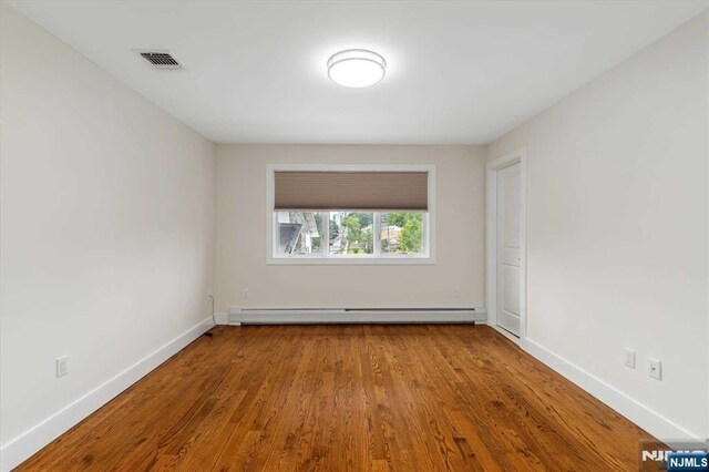 spare room featuring baseboards, visible vents, baseboard heating, and wood finished floors