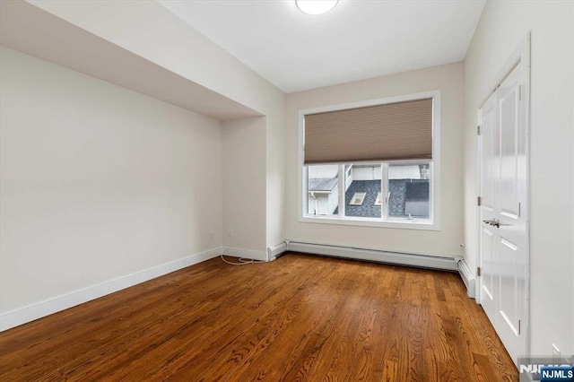 unfurnished room with baseboards, a baseboard heating unit, and wood finished floors