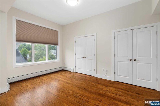 unfurnished bedroom with wood finished floors, two closets, and baseboard heating