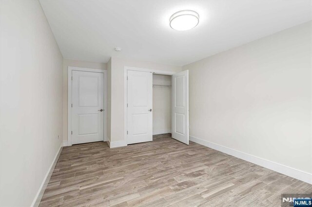 unfurnished bedroom with baseboards, light wood finished floors, and a closet
