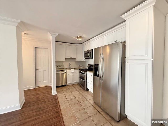 kitchen with light tile patterned floors, white cabinets, ornamental molding, and stainless steel appliances