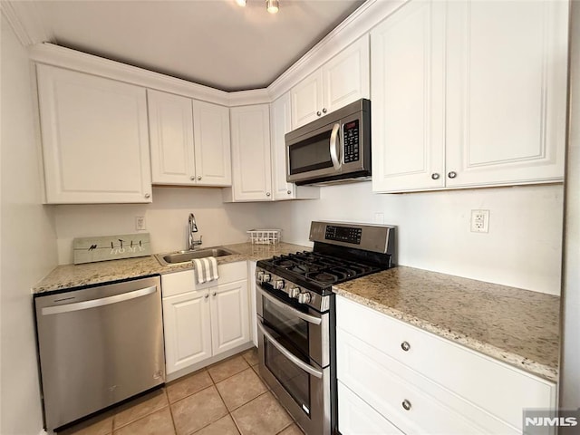 kitchen with light stone countertops, white cabinets, appliances with stainless steel finishes, sink, and light tile patterned flooring