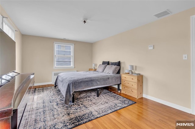 bedroom with radiator, hardwood / wood-style floors, and multiple windows