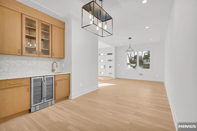 kitchen featuring decorative light fixtures, wine cooler, light hardwood / wood-style floors, sink, and backsplash