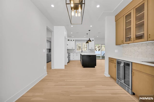 kitchen featuring light brown cabinets, wine cooler, backsplash, hanging light fixtures, and light wood-type flooring