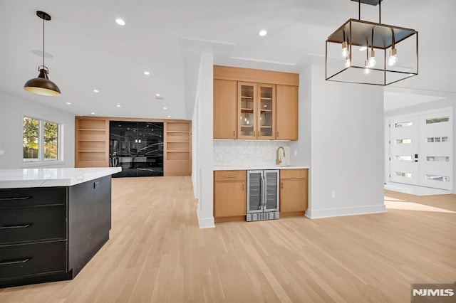 kitchen featuring tasteful backsplash, sink, light hardwood / wood-style flooring, hanging light fixtures, and beverage cooler