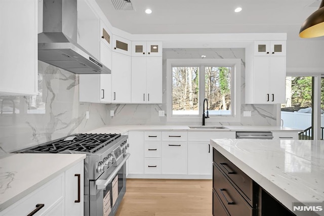 kitchen featuring high end stainless steel range oven, wall chimney exhaust hood, and white cabinets