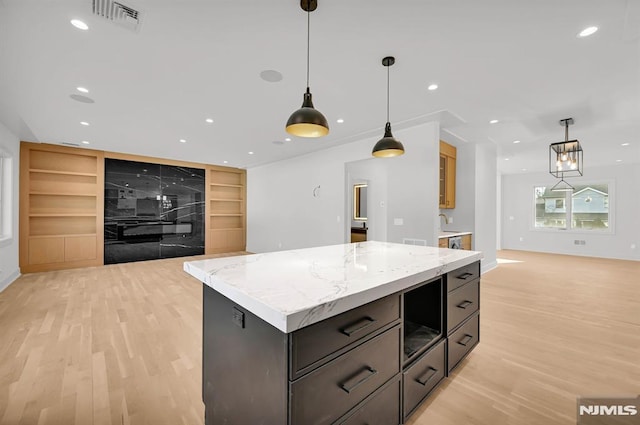 kitchen with built in shelves, light stone countertops, a kitchen island, and pendant lighting