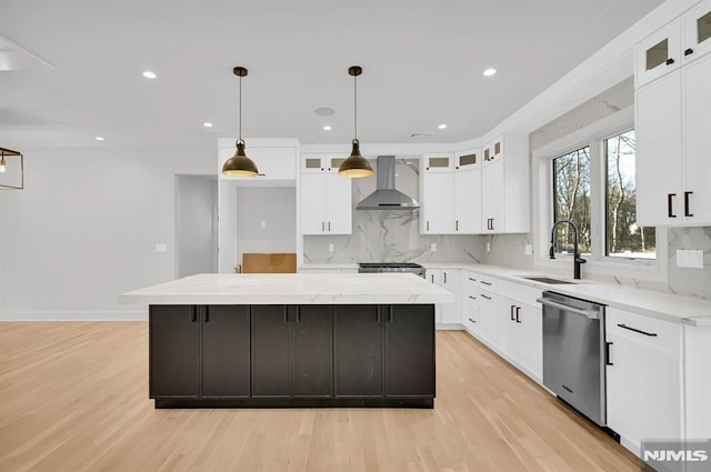 kitchen with dishwasher, wall chimney range hood, a center island, sink, and white cabinets