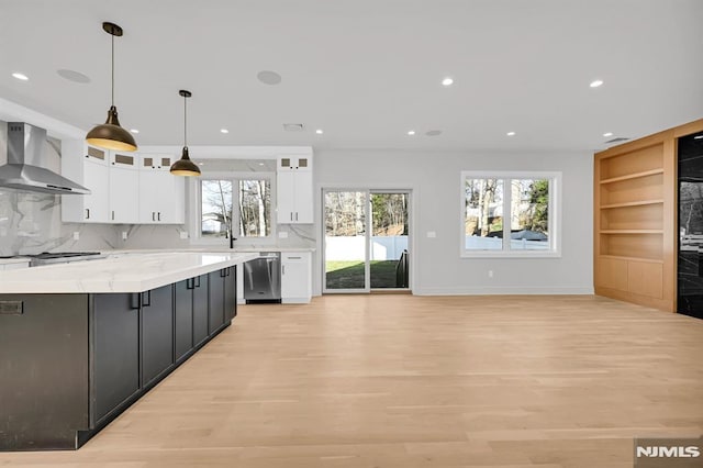 kitchen featuring appliances with stainless steel finishes, decorative light fixtures, white cabinetry, wall chimney range hood, and tasteful backsplash