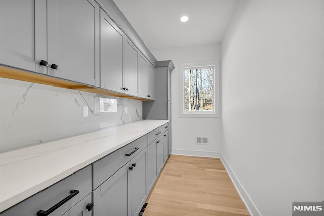 bar featuring gray cabinetry, light hardwood / wood-style floors, light stone counters, and backsplash