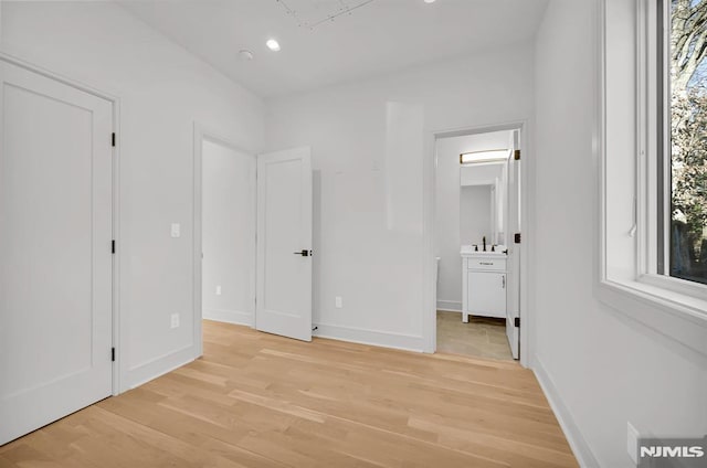 unfurnished bedroom featuring multiple windows, light hardwood / wood-style flooring, and connected bathroom