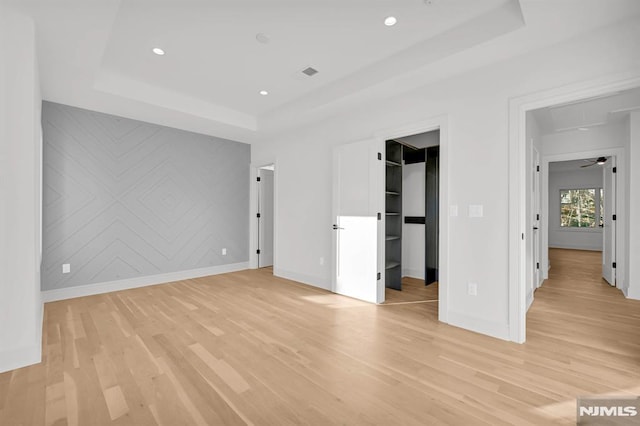 unfurnished bedroom with a tray ceiling, a closet, a walk in closet, and light wood-type flooring